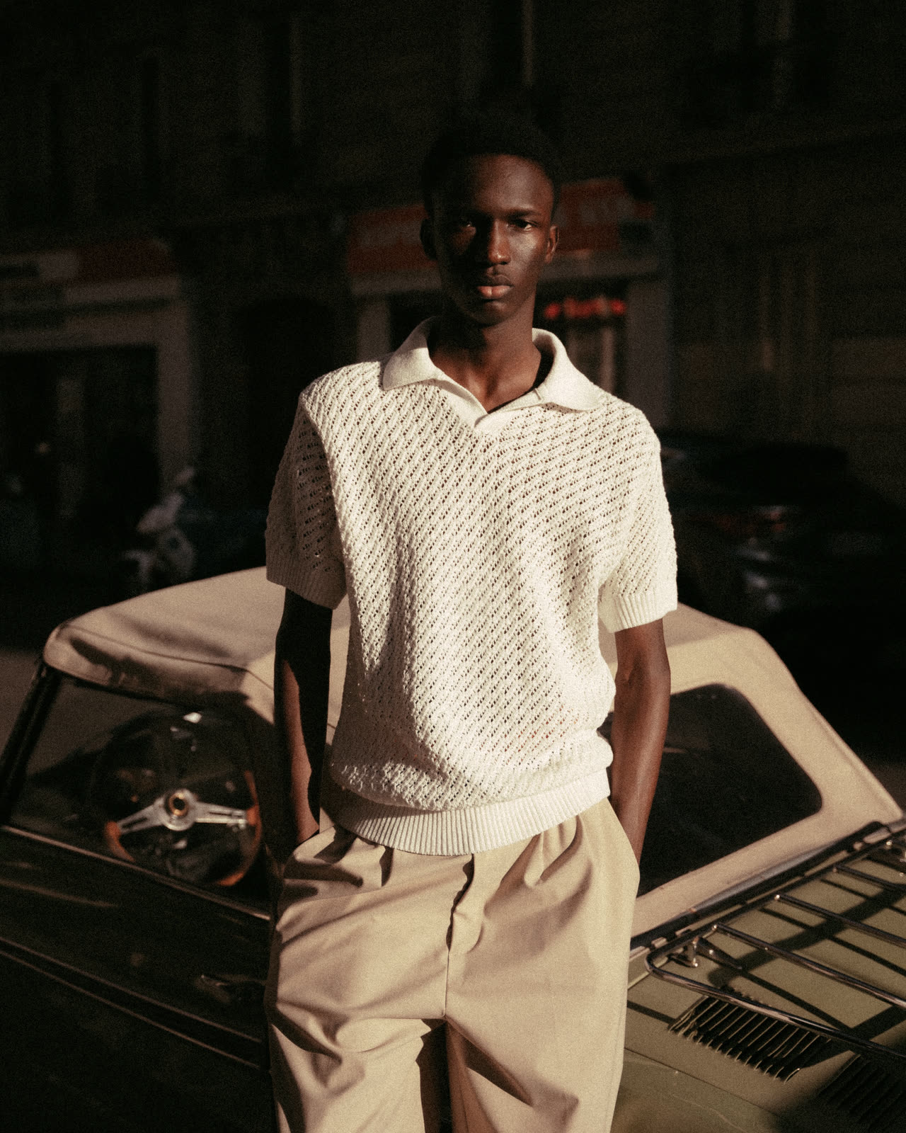 Mannequin en polo crochet crème devant une voiture ancienne, lumière du soir